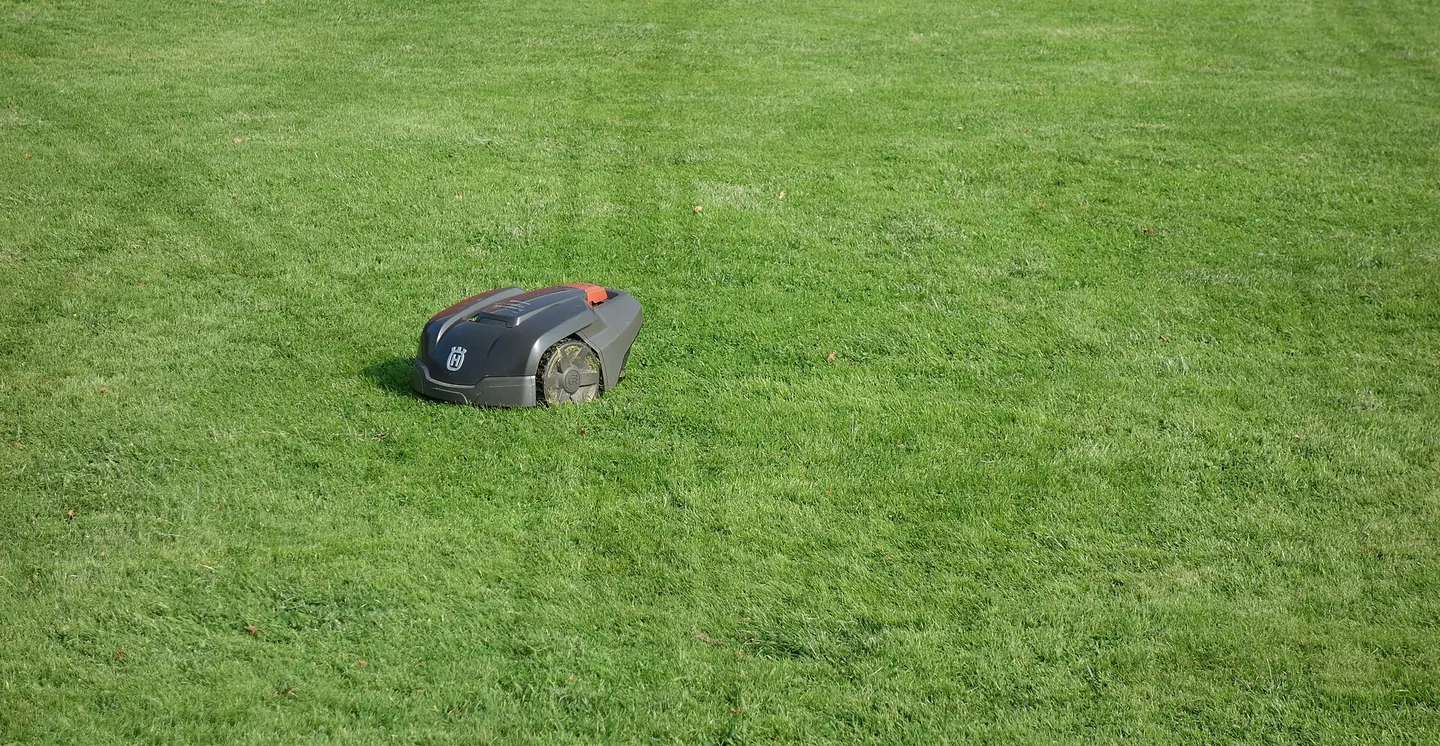 En robotgräsklippare kör på en klippt gräsmatta med synliga körspår efter sig.